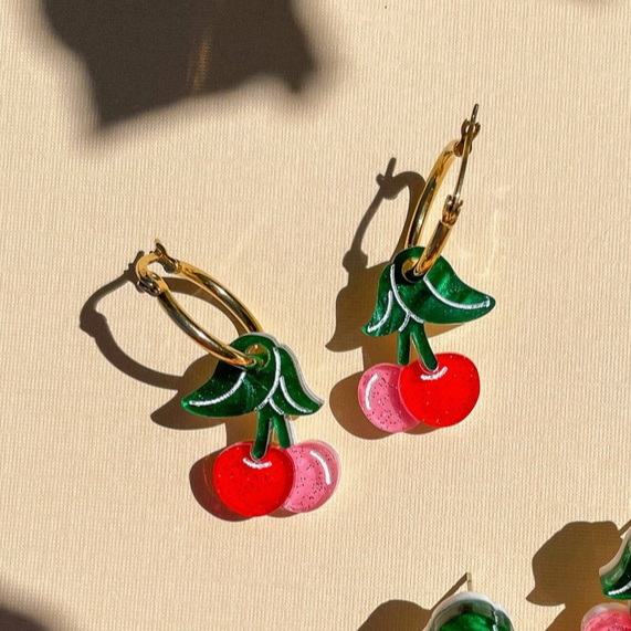 Cherry-themed earrings on a beige background