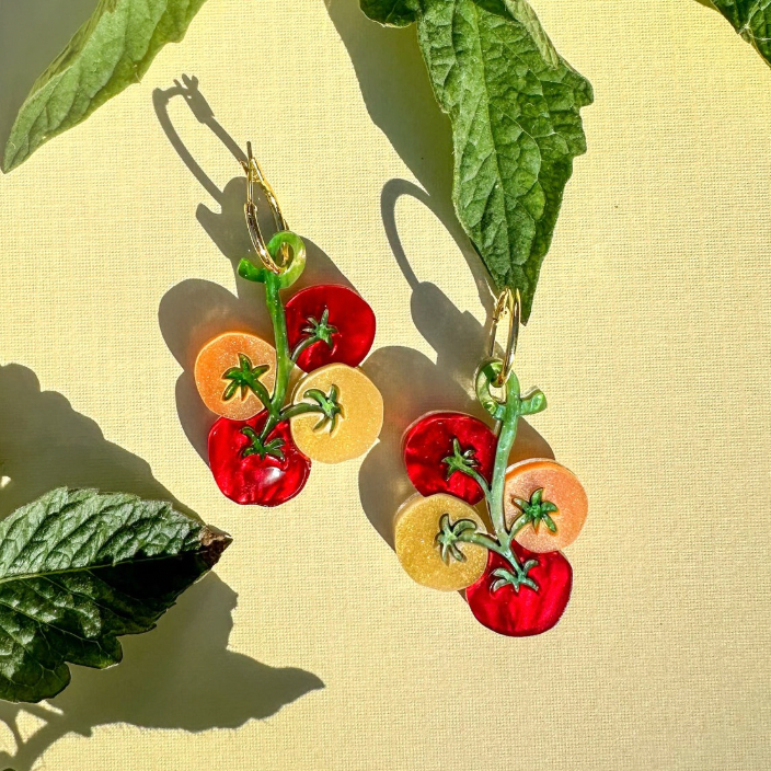Tomato-shaped earrings with green stems on a yellow background with green leaves.