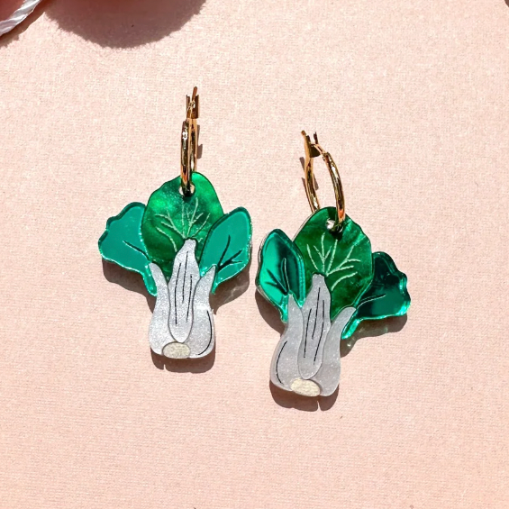Pair of green leaf-shaped earrings on a light pink background with colorful pom-poms.