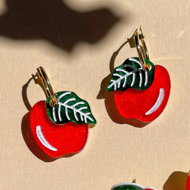 Red apple-shaped earrings with green leaves on a beige background